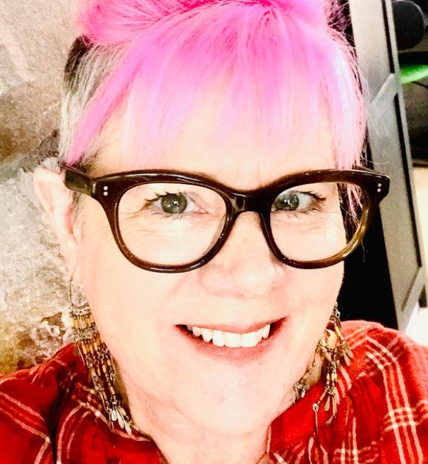 A woman with pink hair and glasses smiling